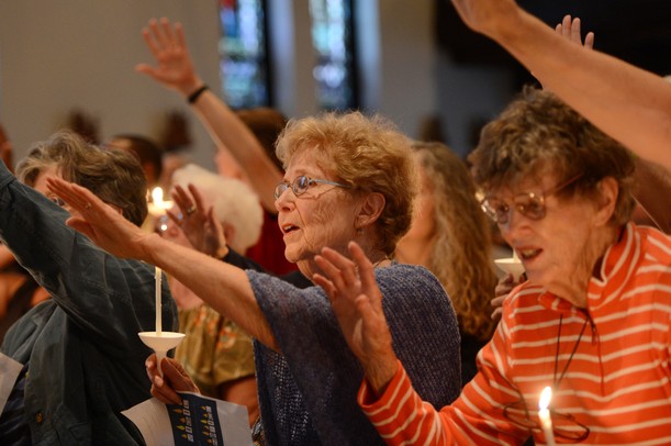Sara King, of Ann Arbor, raises her arm and sings during a prayer vigil in support of Camp Take Notice at St. Mary Student Parish on Thursday night. Melanie Maxwell I AnnArbor.com